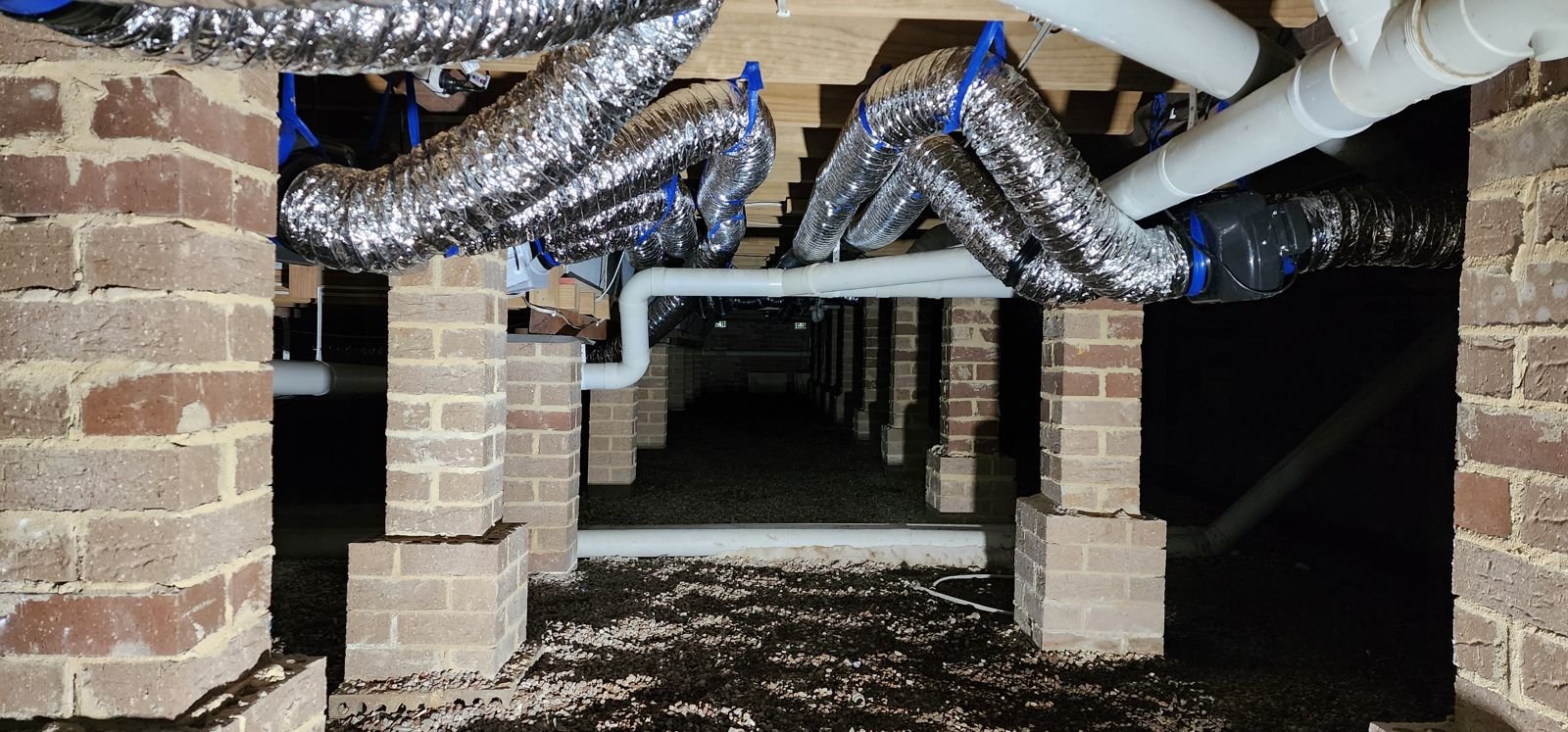 Silver ducting run between brick piers under an older home