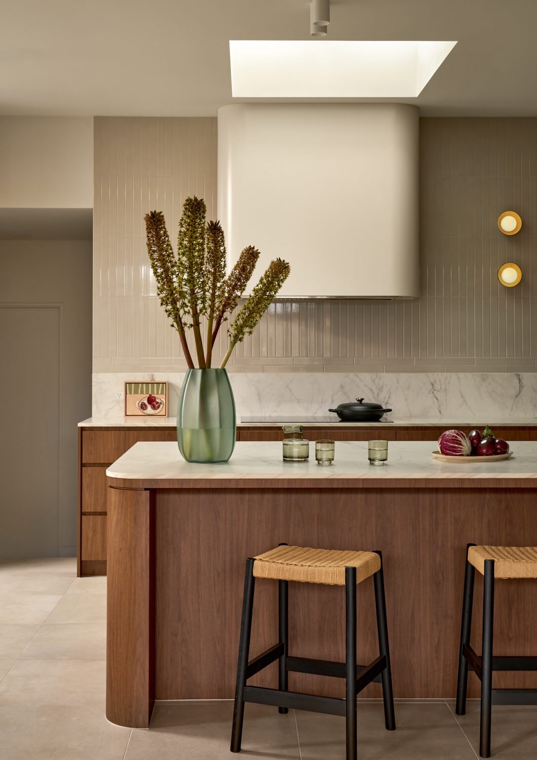 The island bench and curved range hood under the skylight, with two round wall lights beside the hood