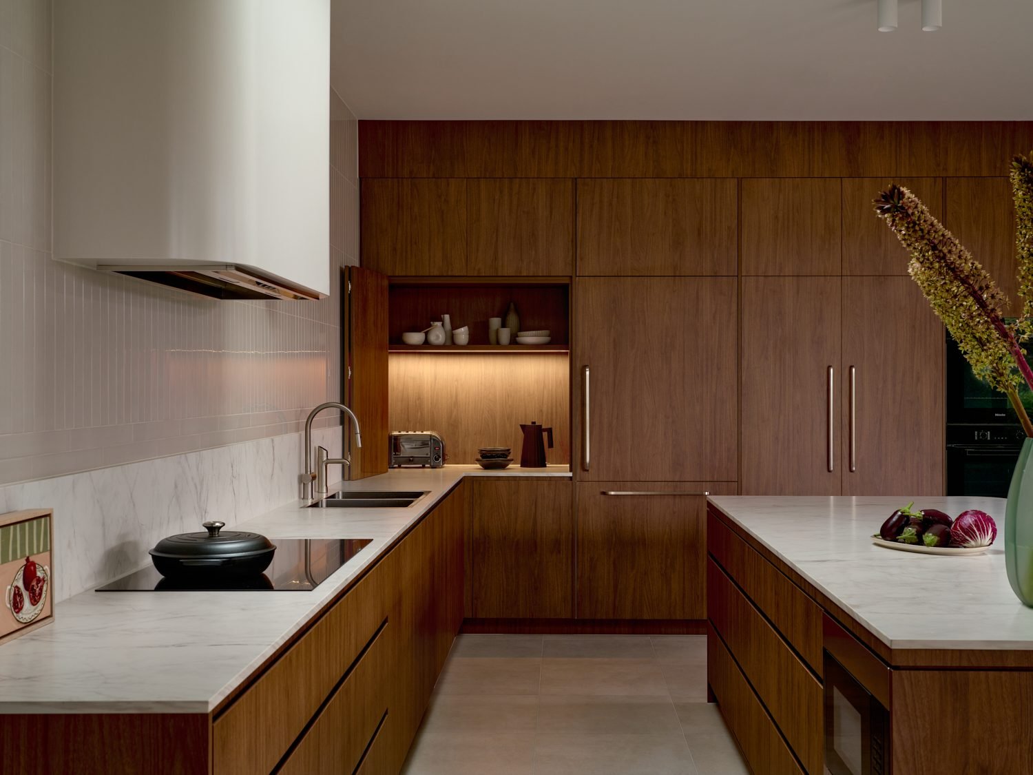 Walnut kitchen with a curved range hood and a lit open shelf set into the joinery
