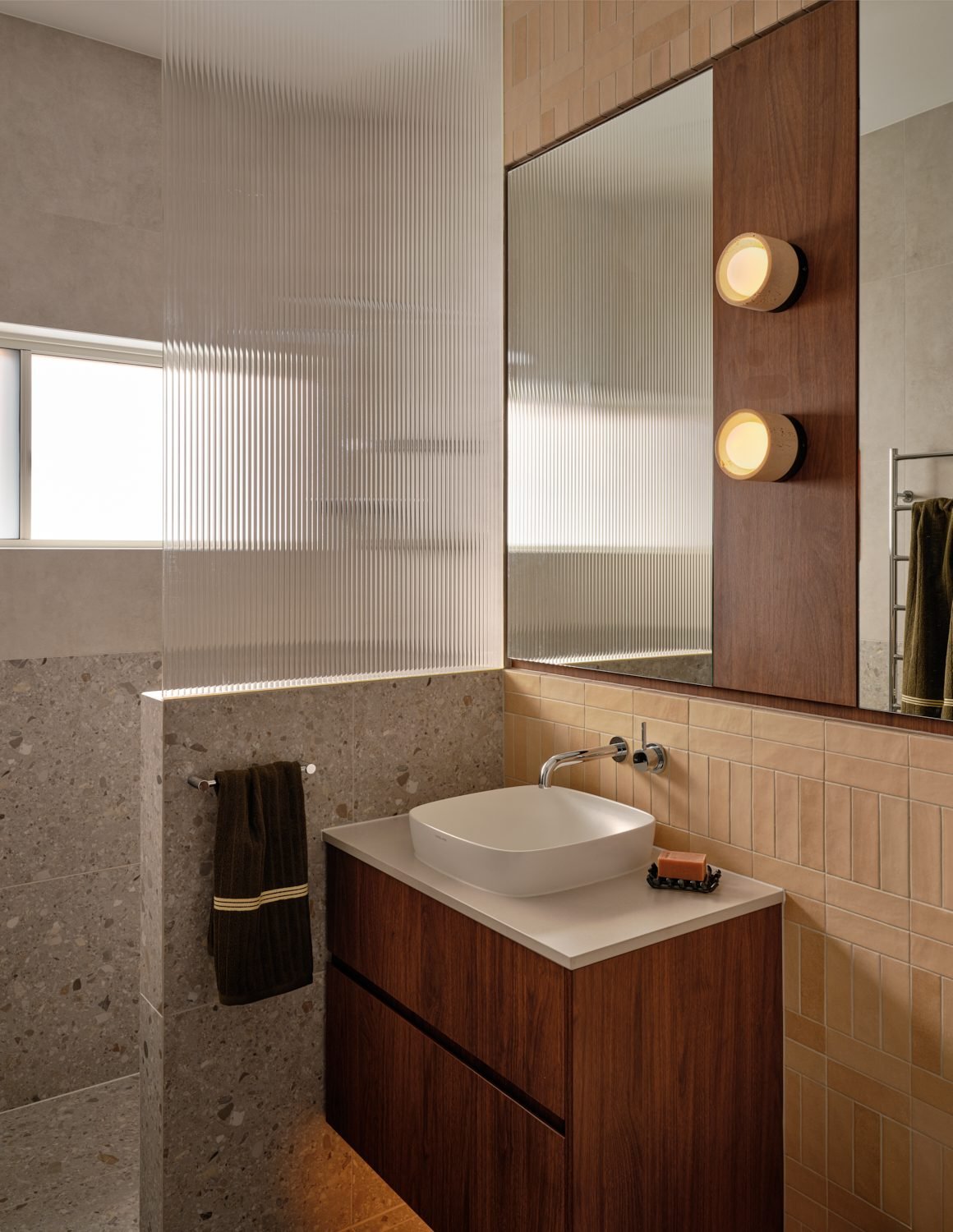 Bathroom vanity with two round wall lights beside the mirror and a fluted glass shower screen