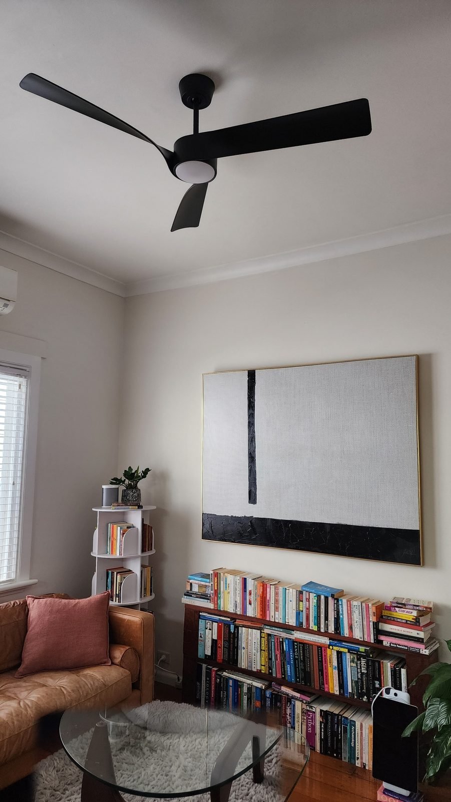 Black fan with a light under a high living room ceiling, bookshelf below