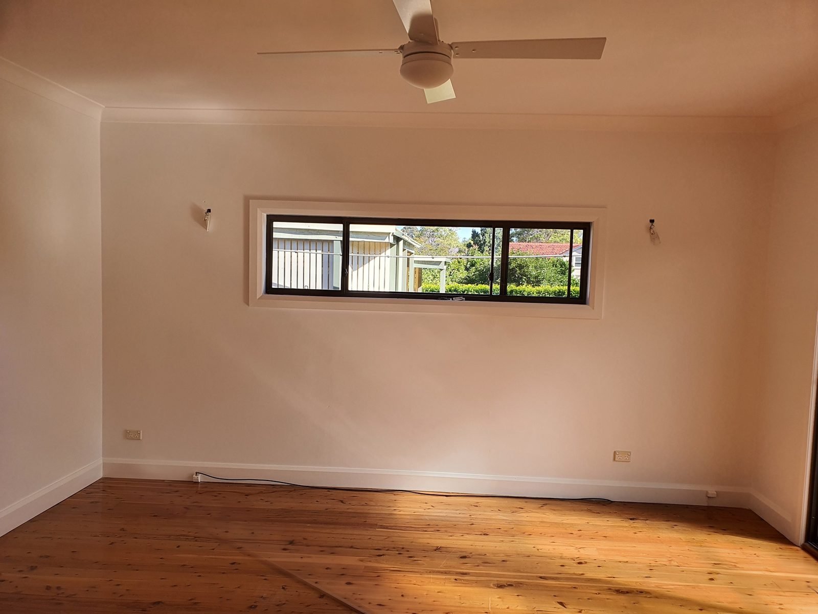 White fan in an empty, freshly painted room with timber floors