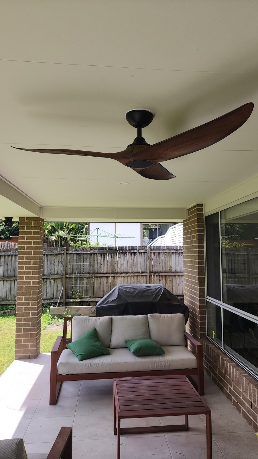 Dark timber-look ceiling fan above an outdoor lounge on a brick-pillared patio