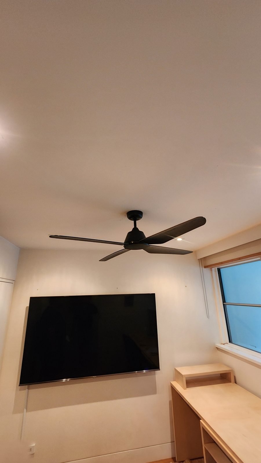 Matte black three-blade fan above a desk and wall-mounted screen