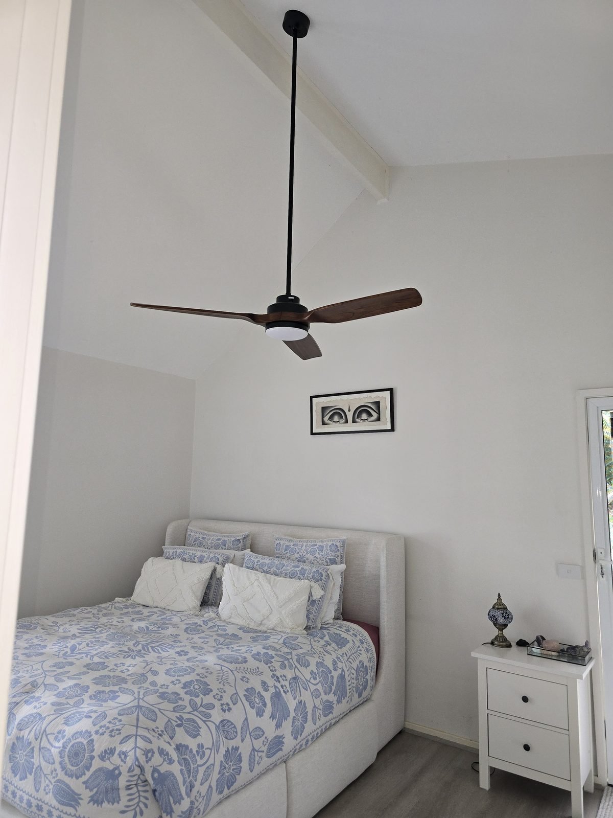 Timber-look fan on a long drop rod above a bed under a sloping ceiling