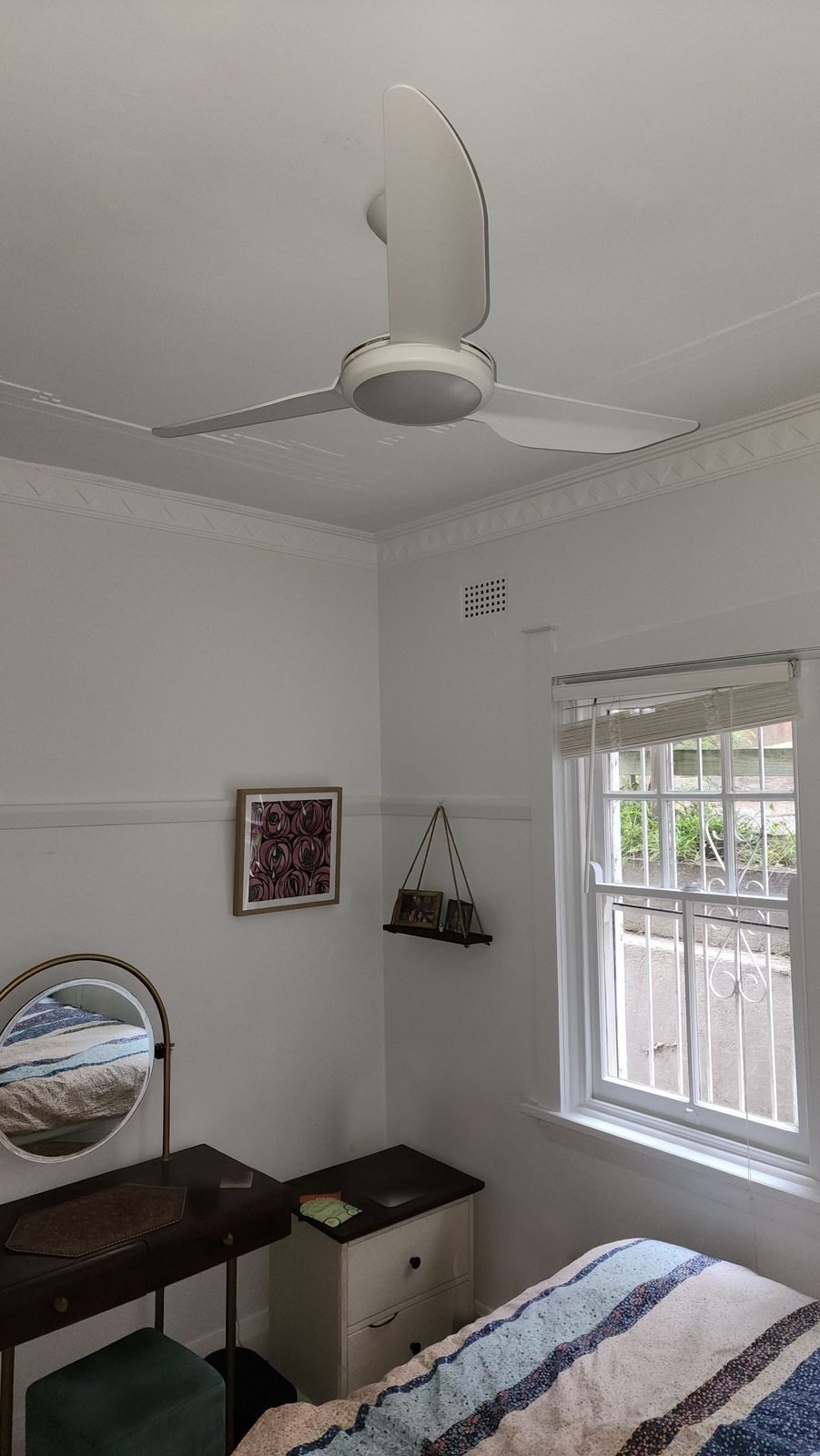 White fan with a light in the centre, above a bed beside a window