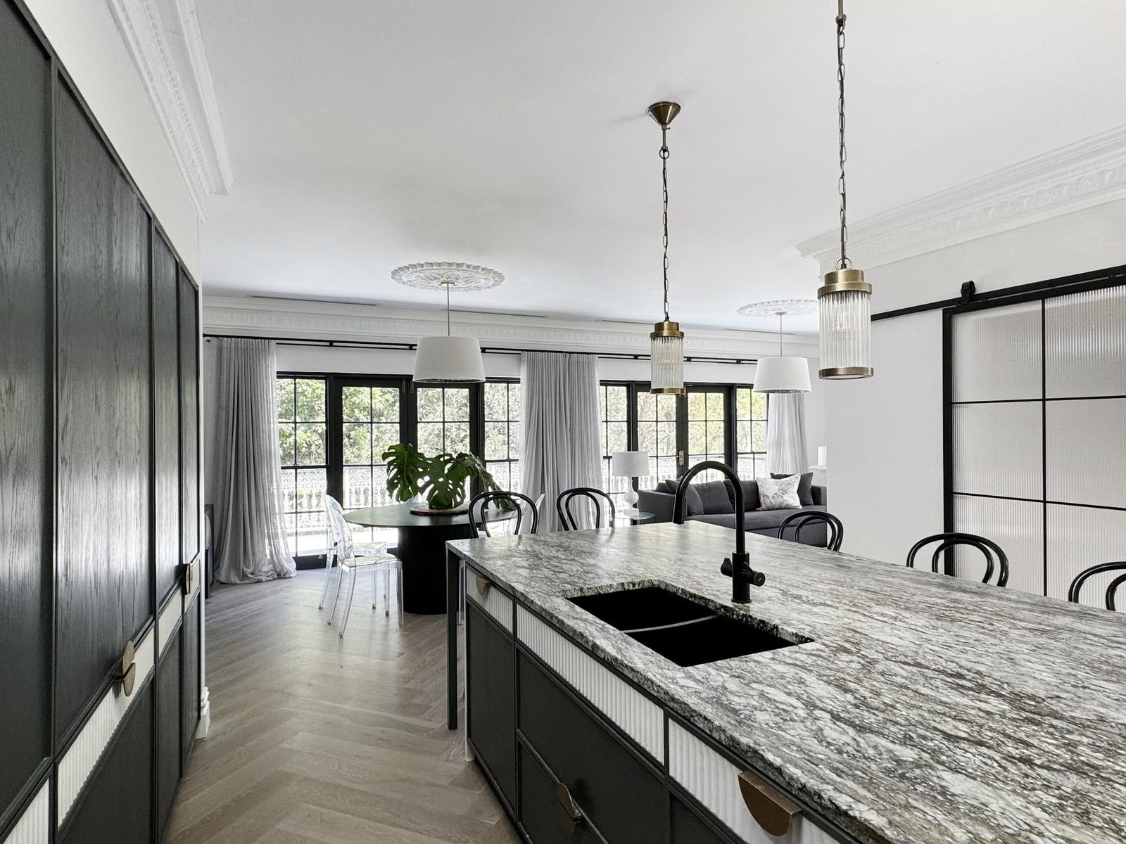 Long stone island with glass and brass pendants, dark timber cabinetry behind