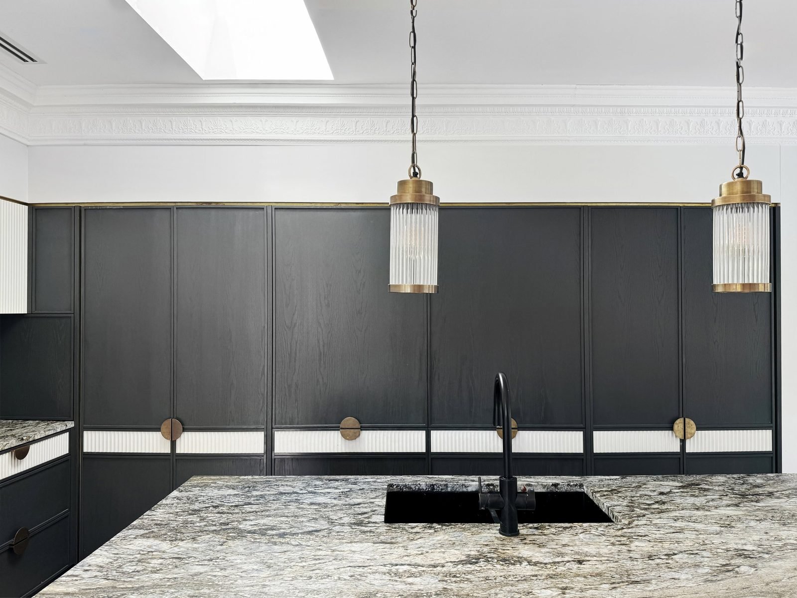 Two glass pendants above the island, one either side of a black tap and sink