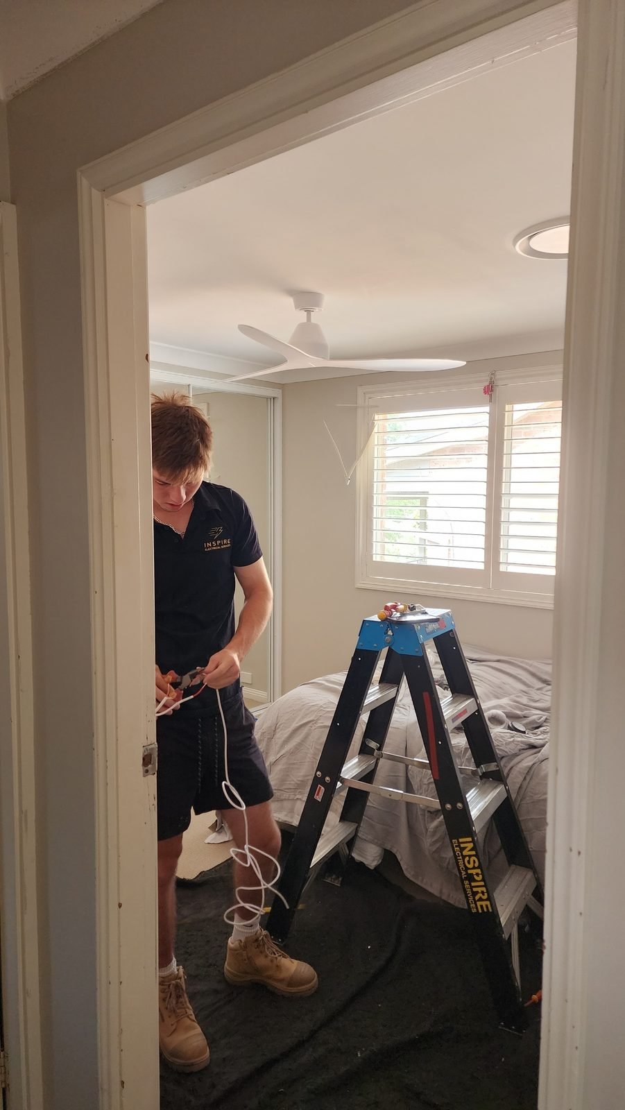 An electrician in a bedroom doorway preparing wiring beside a step ladder
