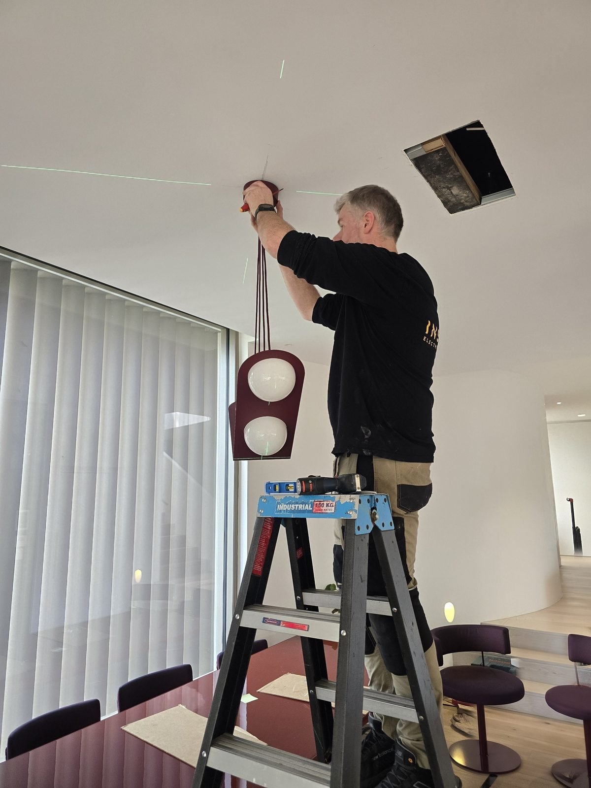 An electrician on a ladder hanging a pendant over a dining table