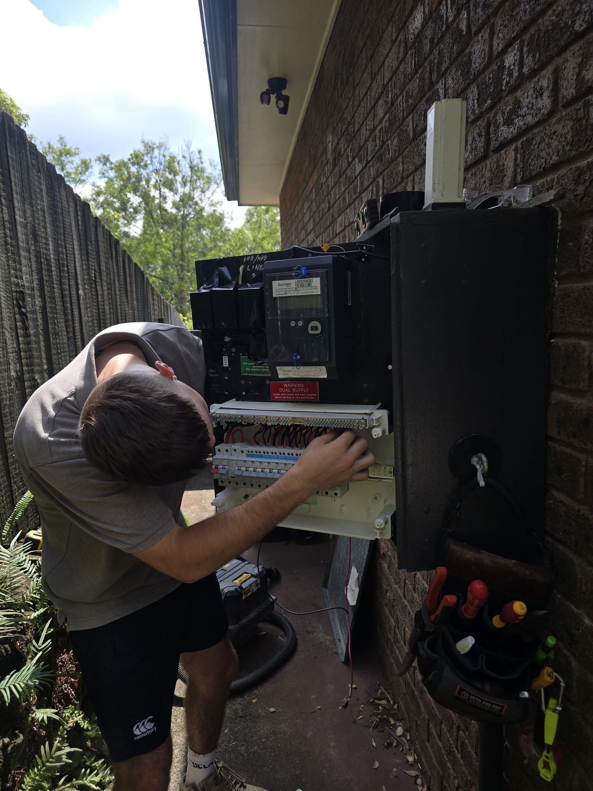 An electrician working inside an open switchboard on a brick wall