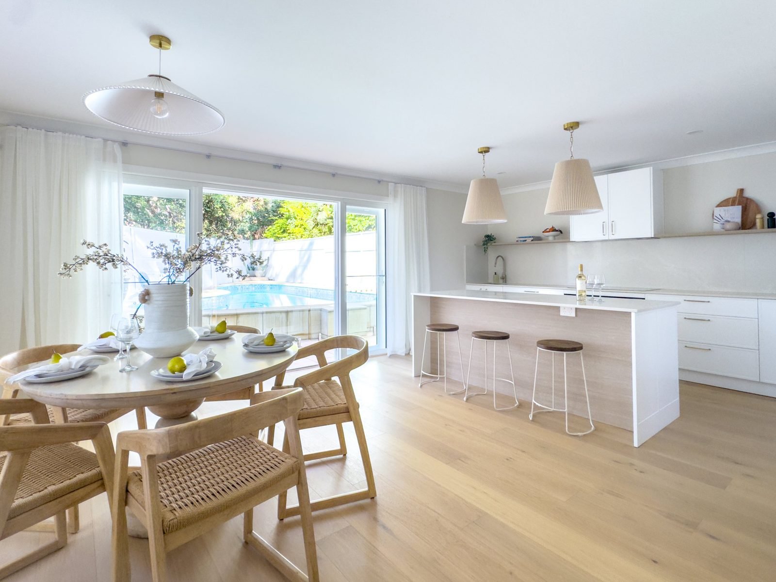 Open-plan dining and kitchen with a pleated pendant over a round table and two over the island