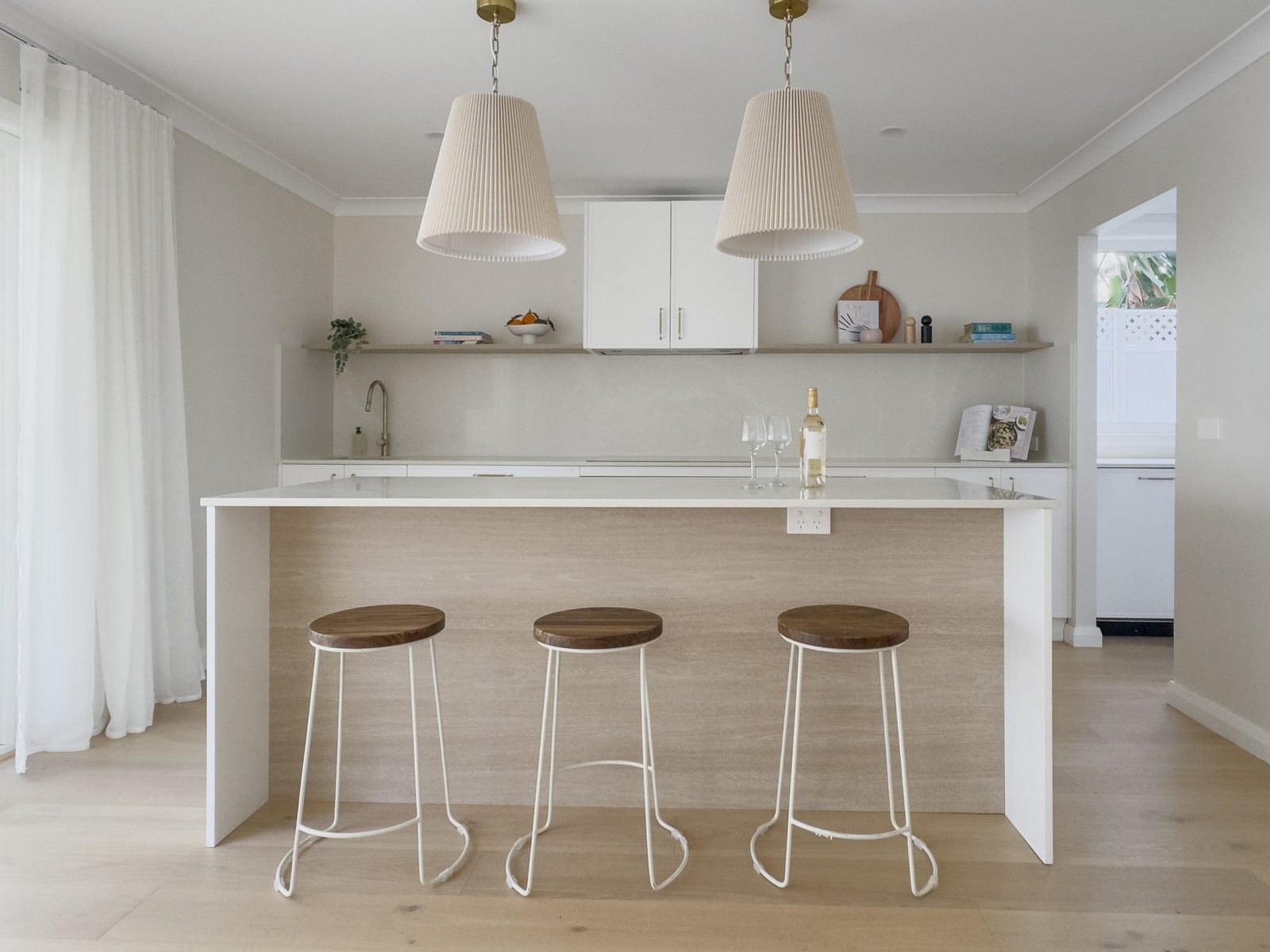 Two pleated pendants above a white island bench with three timber stools