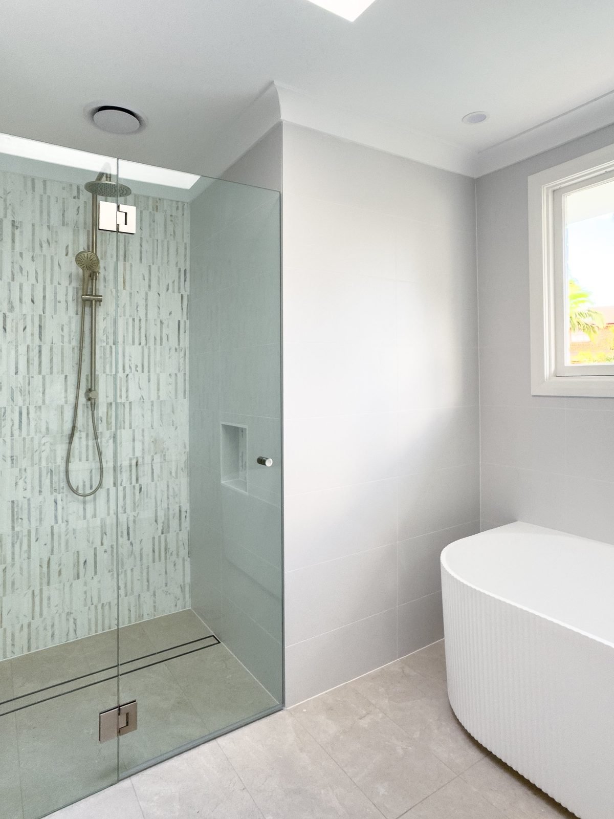 Shower with a ceiling exhaust fan above it and a freestanding bath