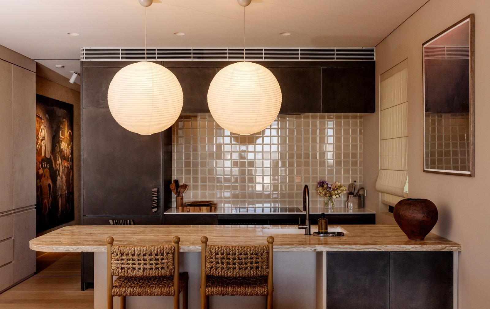 Two paper globe pendants over a stone kitchen bench with woven stools, tiled splashback behind