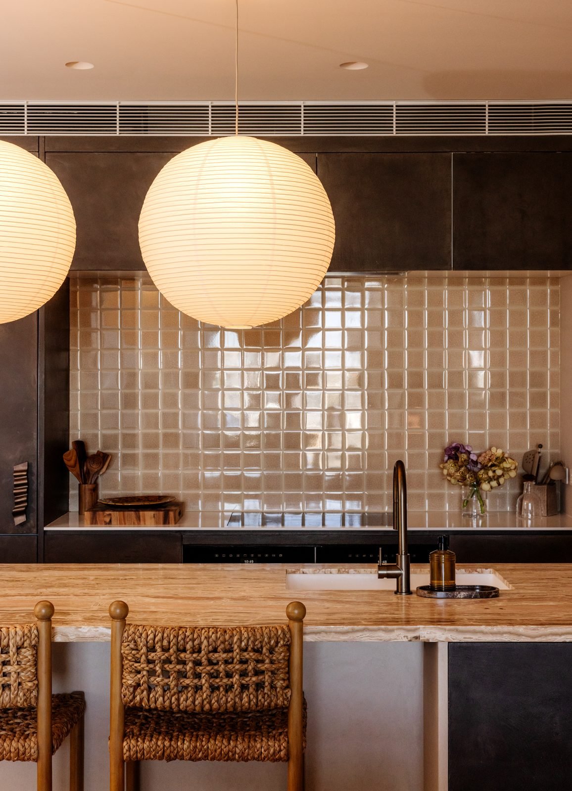 A paper globe pendant in front of a glossy tiled splashback, downlights in the ceiling