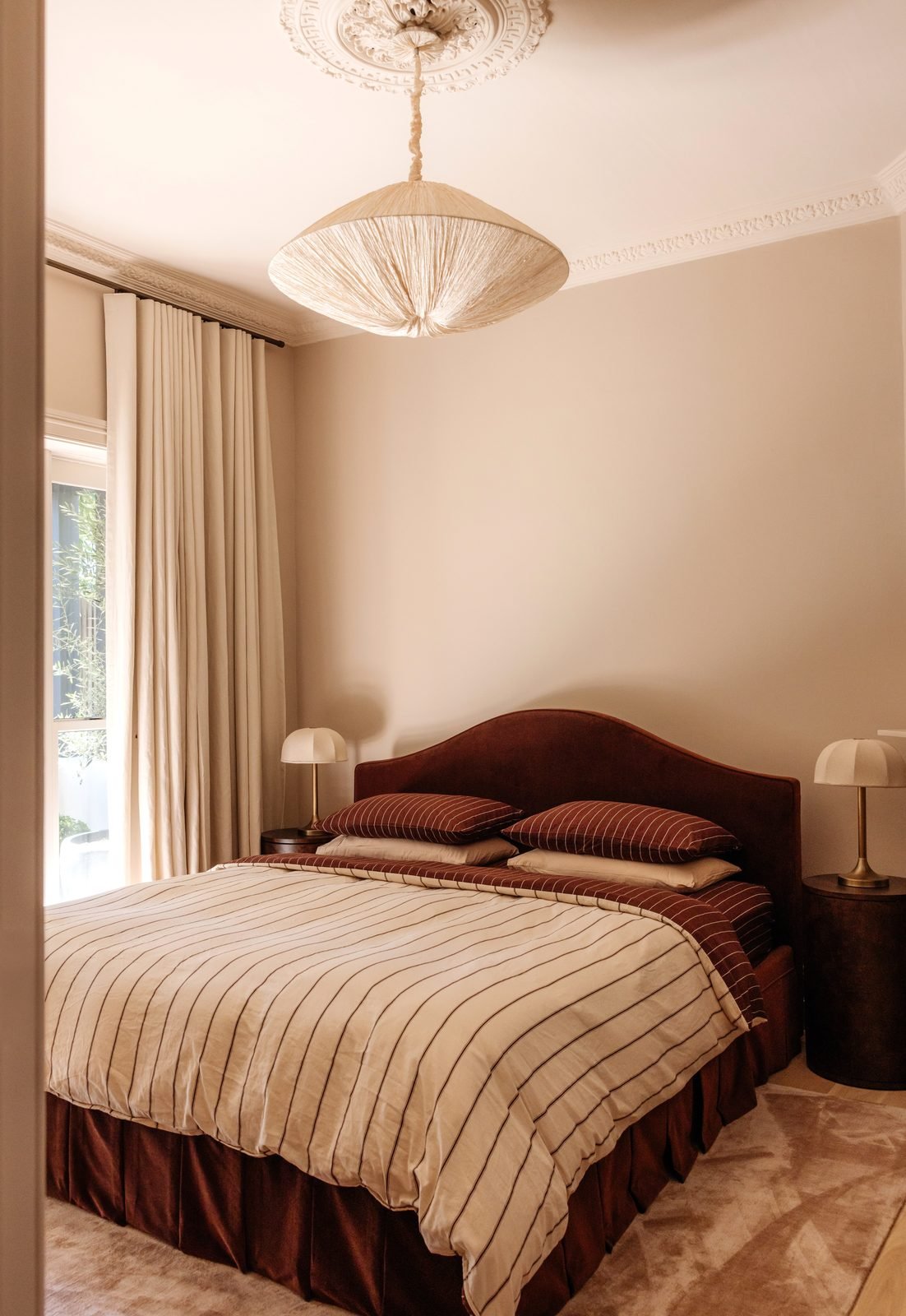 A pleated pendant hanging from an ornate ceiling rose above a bed