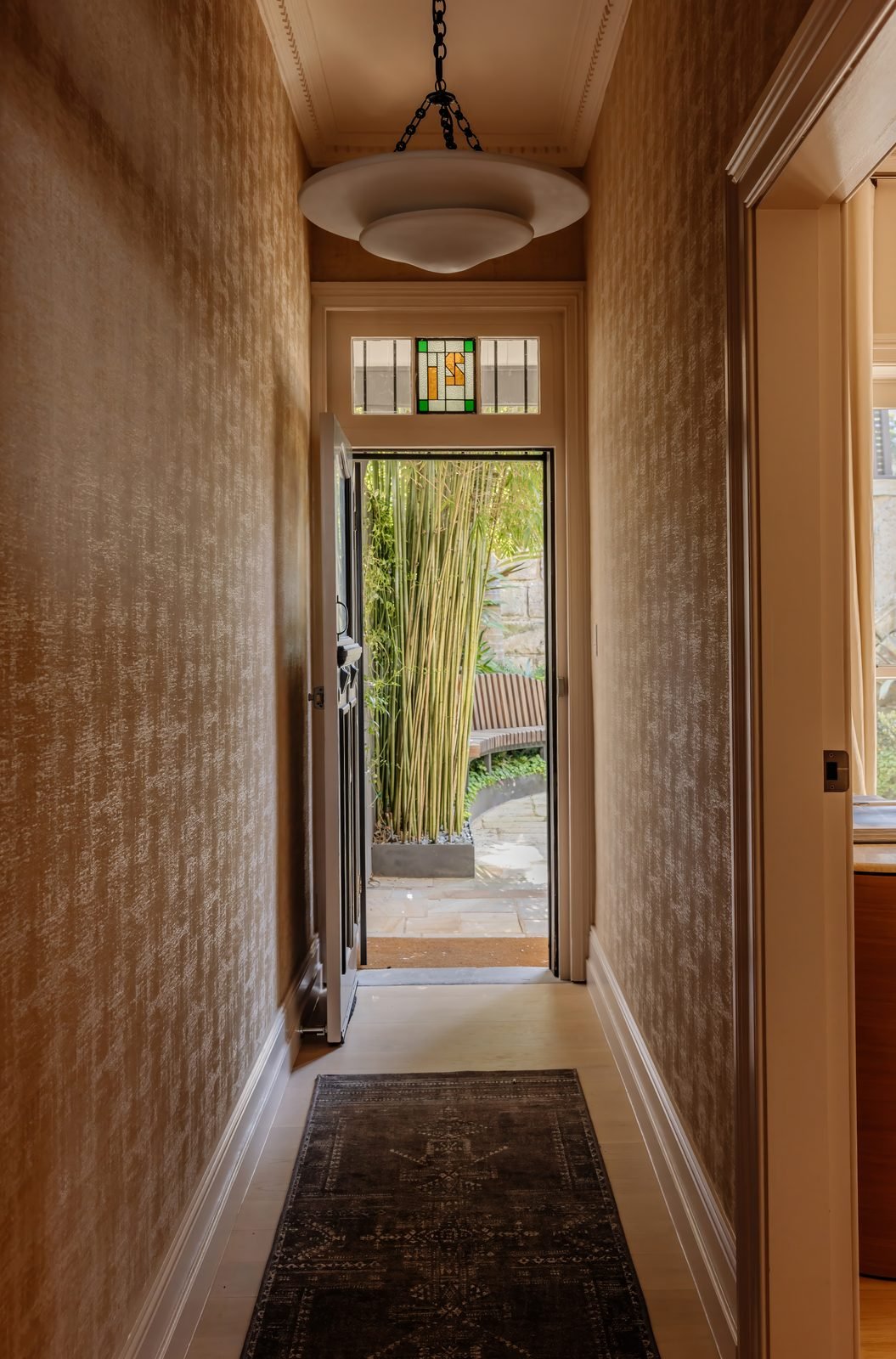 A pendant light in a narrow hallway, looking out through the open front door