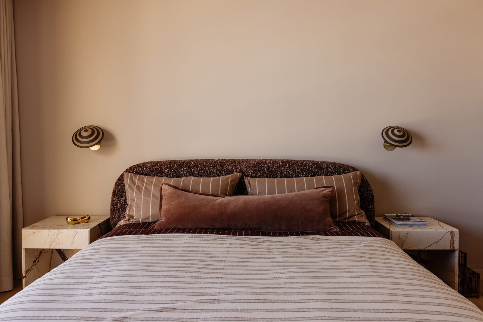 A pair of striped wall sconces either side of a bed with marble bedside tables