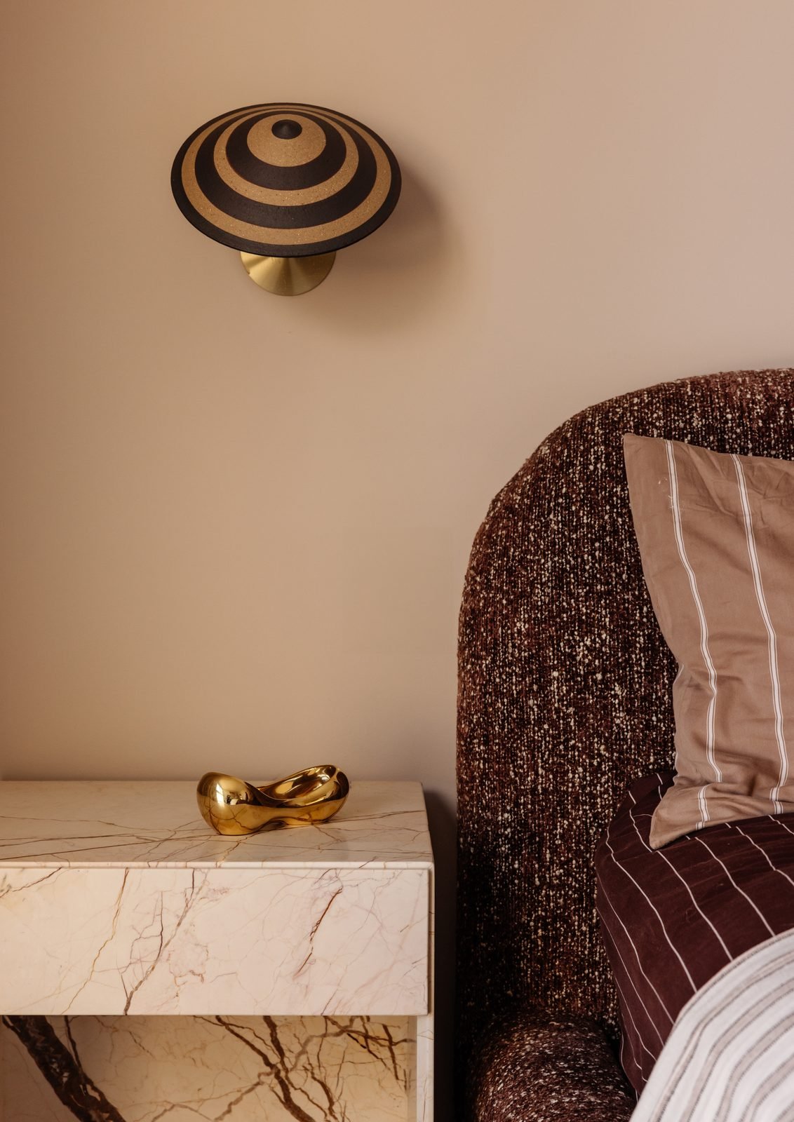 Close view of a striped wall sconce above a marble bedside table