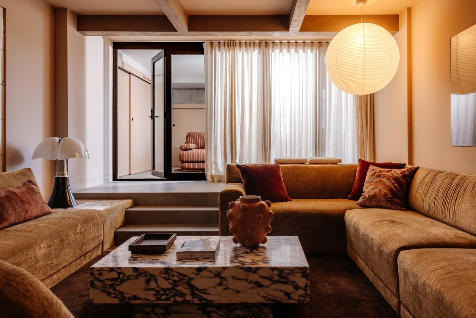 A paper globe pendant above a sunken lounge with a marble coffee table